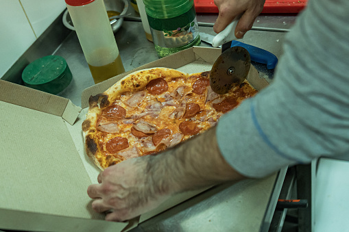Close up of male hands slicing freshly baked pizza with round cutter wheel. Unrecognizable male hands.