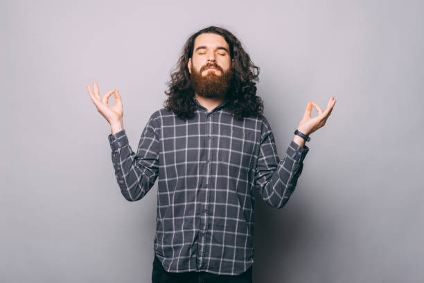 istock Young man in checkered shirt making zen gesture over grey background 1358758757