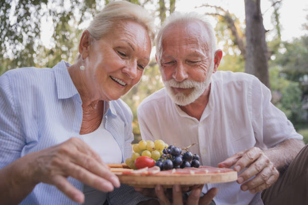 istock Happy elderly couple choosing fruit from a fruit plate on a picnic 1358760040