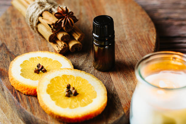 Simple christmas aromatherapy still life with a small essential oil bottle and anise star, cinnamon sticks, oranges with clove spice and a lighted candle stock photo