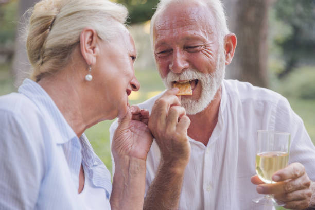 istock Mature married couple snacking crackers and drinking white wine on a picnic 1358760282
