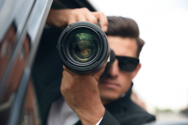 istock Private detective with camera spying from car, focus on lens 1358760321