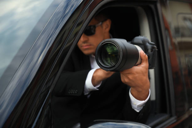 istock Private detective with camera spying from car, focus on lens 1358760360