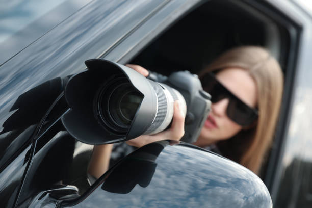 istock Private detective with camera spying from car, focus on lens 1358761277