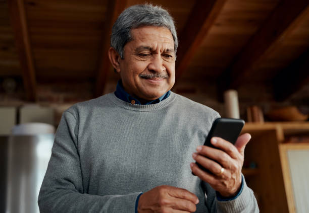 istock Smiling multi-cultural elderly male reading a message on smartphone while standing in modern kitchen 1358761667