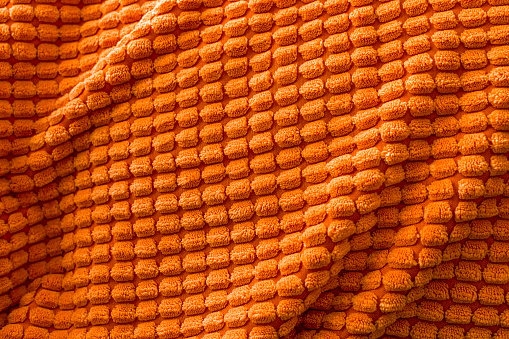 Texture of orange soft fleecy blanket textile with twisted folds