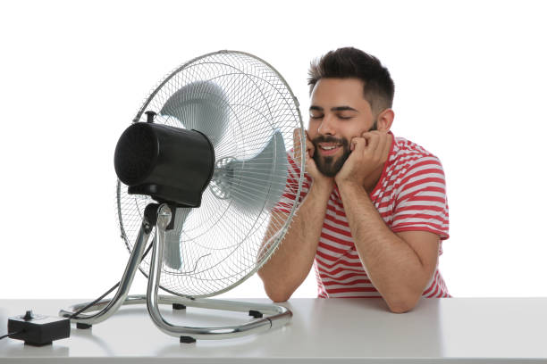 istock Man enjoying air flow from fan on white background. Summer heat 1358763626