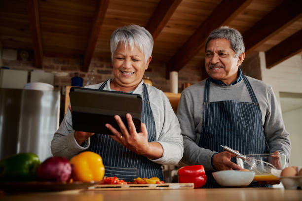 istock Smiling multi-cultural elderly couple using tablet to follow recipe in modern kitchen. Happy couple cooking healthy meal 1358763858