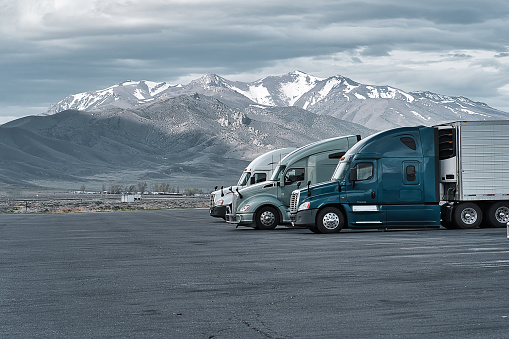 Commercial trucks parked at a truck stop in Nevada with mountain covered in snow seen in the background.