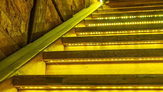 Yellow led light pouring from below onto a wooden staircase. Space for text. Abstract background. Image for design.