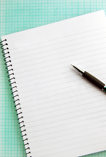 One pen  placed over a blank empty page of a tilted spiral notepad and graph paper The page is empty and blank for copy space. There is no text and no people.