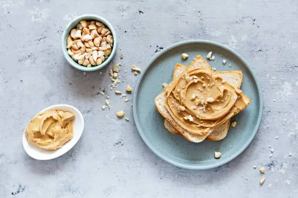 Toast (sandwich) of a slice of toast bread and peanut butter for breakfast on a blue (grey) background.