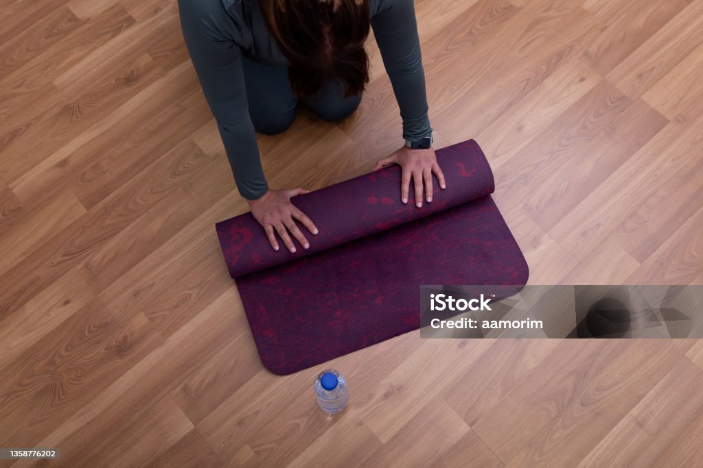 Woman rolling yoga mat Female hands rolling yoga mat with a plastic water bottle nearby 40-44 Years Stock Photo