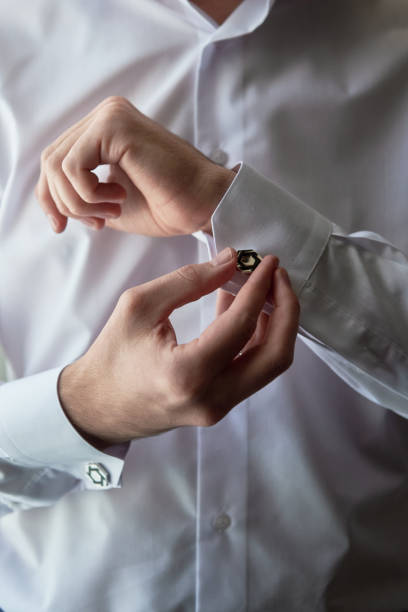 istock Man buttoning cuff link of luxury white shirt sleeve, copy space. Groom fixes cufflinks standing near window, close up 1358777633