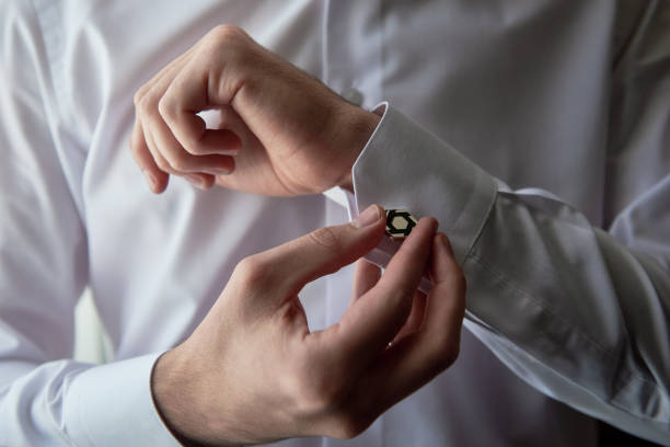 istock Man buttoning cuff link of luxury white shirt sleeve, copy space. Groom fixes cufflinks standing near window, close up 1358777635