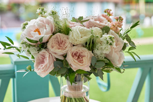 Close up of bridal bouquet of pink and white peony roses and greenery in glass vase on table outdoors, copy space. Wedding concept stock photo