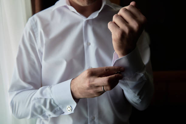 istock Man buttoning cuff link of luxury white shirt sleeve, copy space. Groom fixes cufflinks standing near window, close up 1358780337