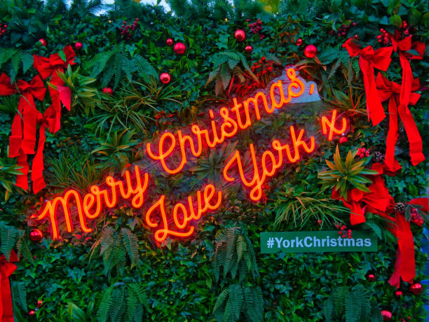 un'insegna al neon rossa illuminata con uno sfondo di fogliame verde offre gli auguri di natale ai visitatori dei mercatini di natale nella città di york, yorkshire, regno unito - single word lighting equipment illuminated photographic effects foto e immagini stock