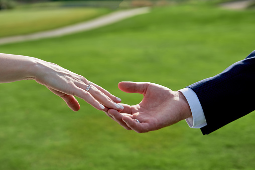 Newlywed couple's hands with wedding rings on golf course background, copy space. Wedding couple, bride and groom, hands with rings, closeup