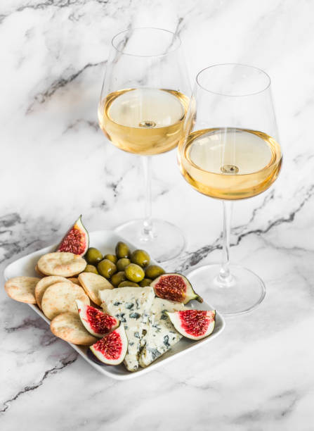 Appetizer plate with blue cheese, olives, homemade cheese cracker, figs  and two glasses of white wine on a light marble background, top view Appetizer plate with blue cheese, olives, homemade cheese cracker, figs  and two glasses of white wine on a light marble background, top view plate fig blue cheese cheese stock pictures, royalty-free photos & images