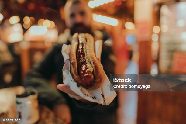 Man Eating A Sausage Hot Dog And Enjoying A Christmas Market Stock Photo - Download Image Now