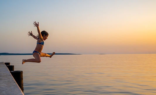 Girl jumping from pier in the water at sunset. Child jumping in the sea in Silba, Croatia.