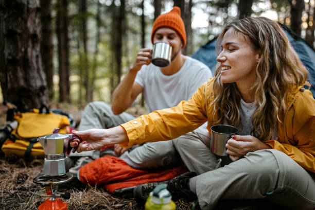 Young couple making coffee during hiking Beautiful and romantic young man and woman preparing hot coffee and tea beverage n portable stove sitting outside tent during hiking adventure tea hot drink stock pictures, royalty-free photos & images