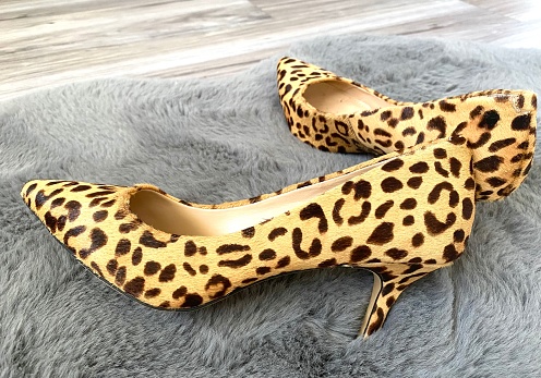 High heeled women’s shoes laying on the floor, shot in natural light on a grey rug. Leopard Print on shoes