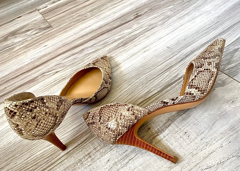 Woman’s high heeled shoes with a snake skin pattern, close up image in natural light against a hard wood floor