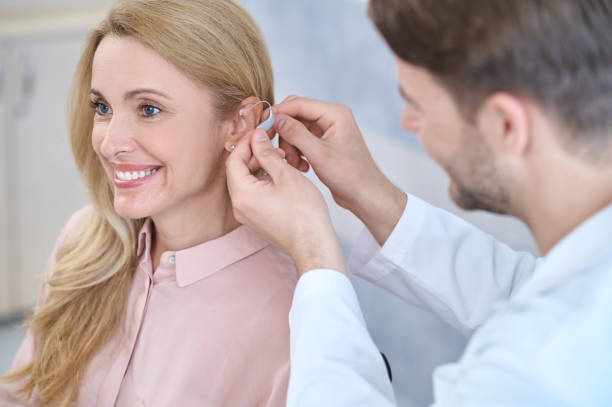 Man putting hearing aid on womans ear stock photo