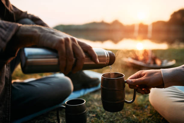 日没時に湖のそばで飲み物を飲む男性のクローズアップ。 - friendship camping night campfire ストックフォトと画像