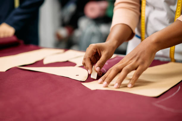istock Close-up of tailor marking pattern with chalk on fabric while working at clothing studio. 1358814137