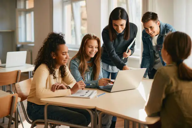 Photo of Happy students using laptop with their computer science professor during a class at high school.