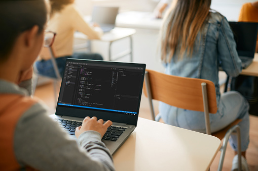 Close-up of student programming while learning computer language on laptop during a class at high school.