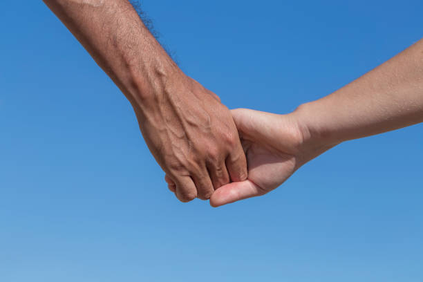 istock Couple hands held together on blue sky background 1358814783