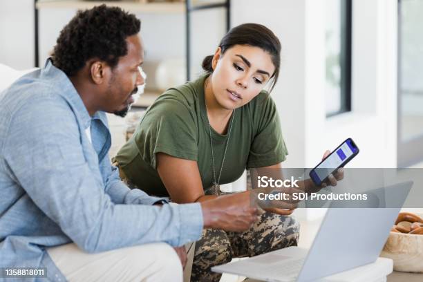 Man And Soldier Wife Discuss Finances Using Phone And Laptop Stock Photo - Download Image Now