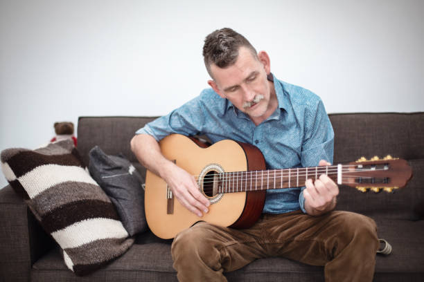 istock man in his 50s sitting on couch and playing guitar 1358821611