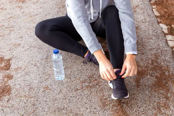 Woman sitting on the floor tying the laces of her sneakers with plastic water bottle next to her