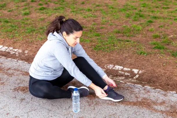 Woman sitting on the floor tying the laces of her sneakers with plastic water bottle next to her