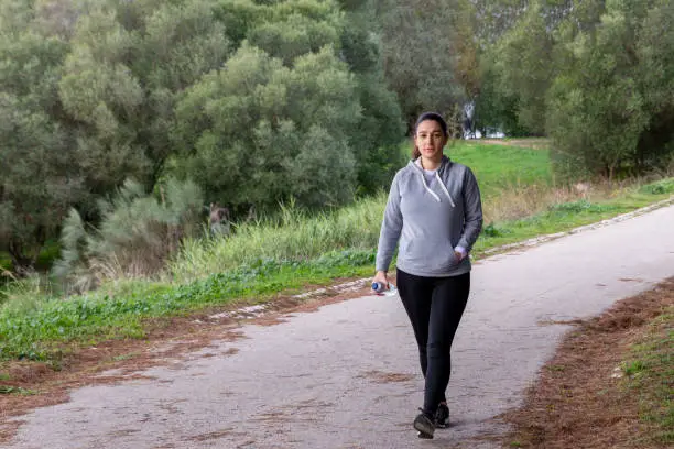 Woman wearing exercise clothes doing her morning fitness routine with a walk in the park. Drinking water from a plastic bottle