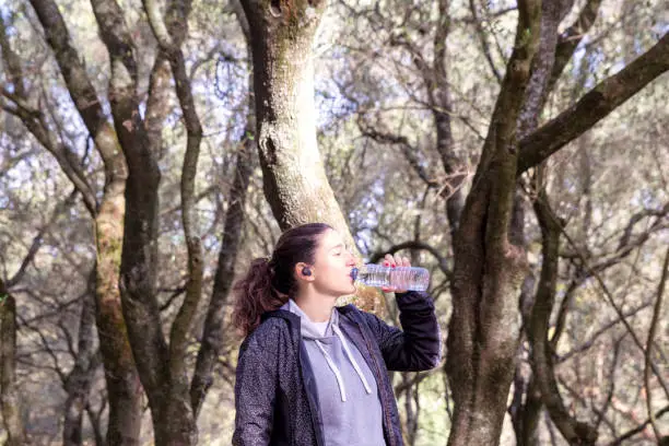 Woman wearing exercise clothes doing her morning fitness routine with a walk in the park. Drinking water from a plastic bottle