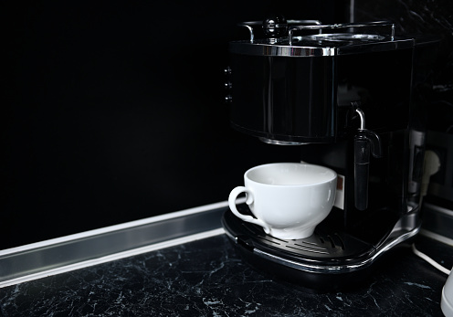 Coffee machine with white ceramic cup at kitchen countertop