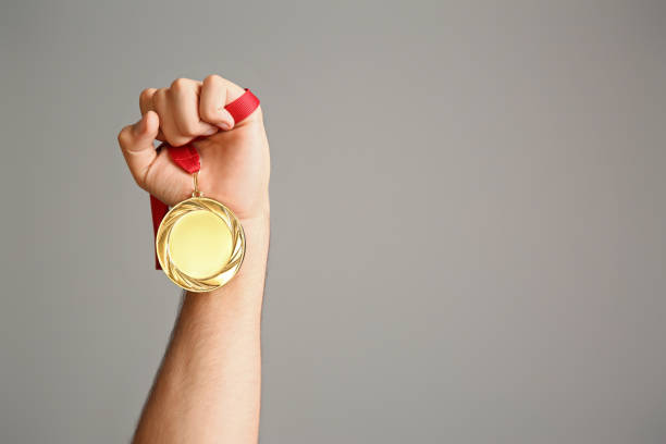istock Man holding golden medal on grey background, closeup. Space for design 1358829232