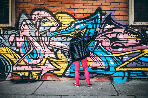 Female street artist painter in respirator mask painting colorful graffiti on wall Modern art, urban concept.