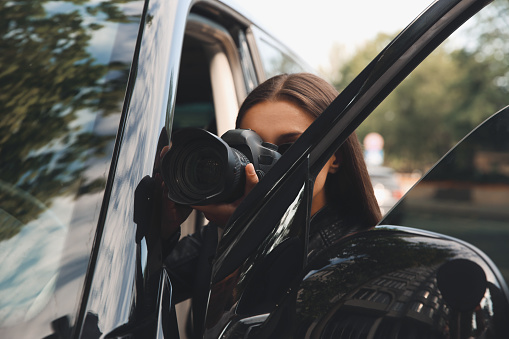Private detective with camera spying near car outdoors