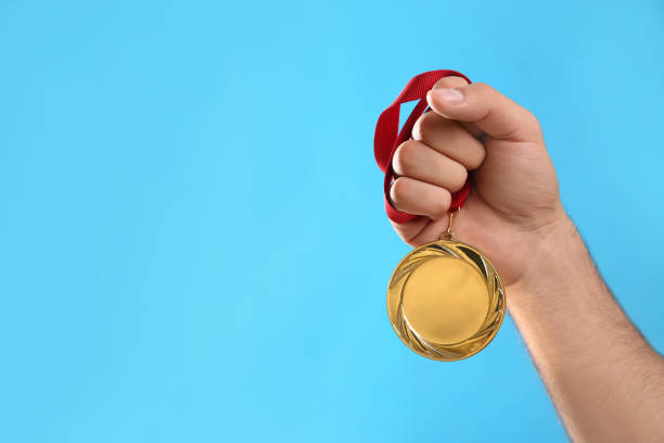 istock Man holding golden medal on light blue background, closeup. Space for design 1358830718