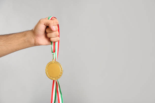 istock Man holding golden medal on grey background, closeup. Space for design 1358830835
