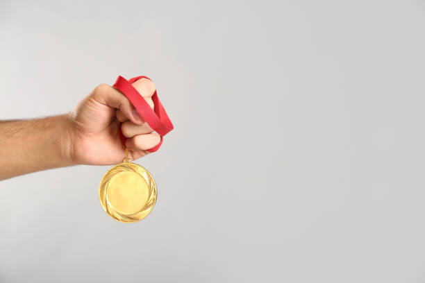 istock Man holding golden medal on grey background, closeup. Space for design 1358831515
