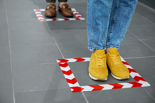 People standing on taped floor markings for social distance, closeup. Coronavirus pandemic