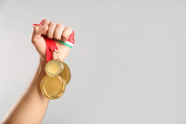 istock Man holding golden medals on grey background, closeup. Space for design 1358831593
